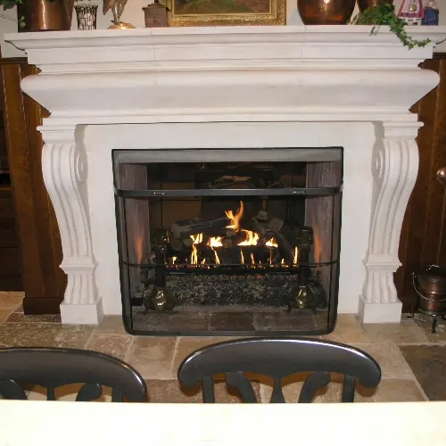 Limestone mantel fireplace with a live gas log fire burning behind a black fire screen