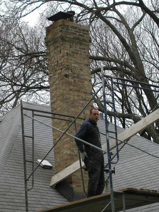 Tradesman on scaffolding beside a tall yellow brick chimney on a slate roof
