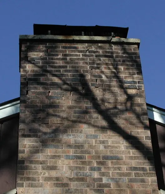Tall brick chimney with cracked mortar joints and open flues, photographed before rebuilding