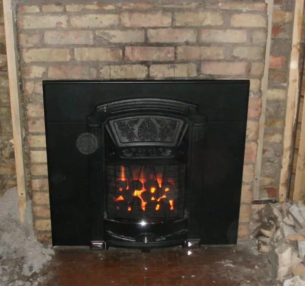 Cast iron gas coal insert with glowing coals set into an exposed brick Victorian fireplace opening