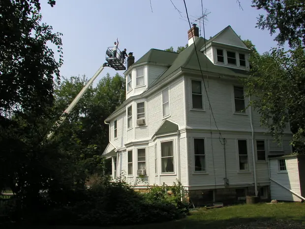Two workers in the basket of a boom lift working at chimney height above a Victorian house