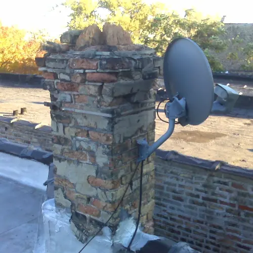 Badly deteriorated common brick chimney on a flat city roof, missing its crown