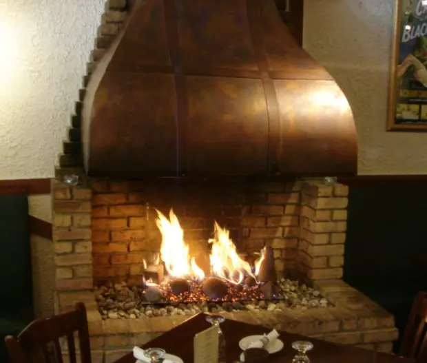 Restaurant fireplace with a copper hood over a brick firebox and tall gas flames